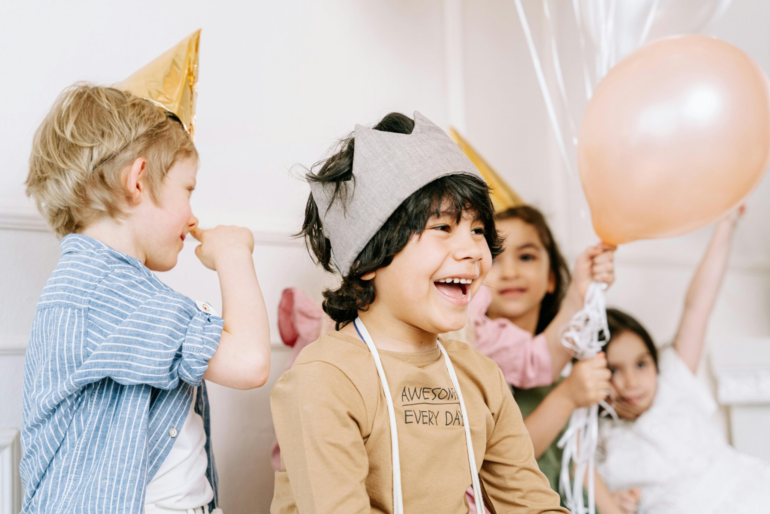 Happy children enjoying a birthday party with balloons and festive hats indoors.